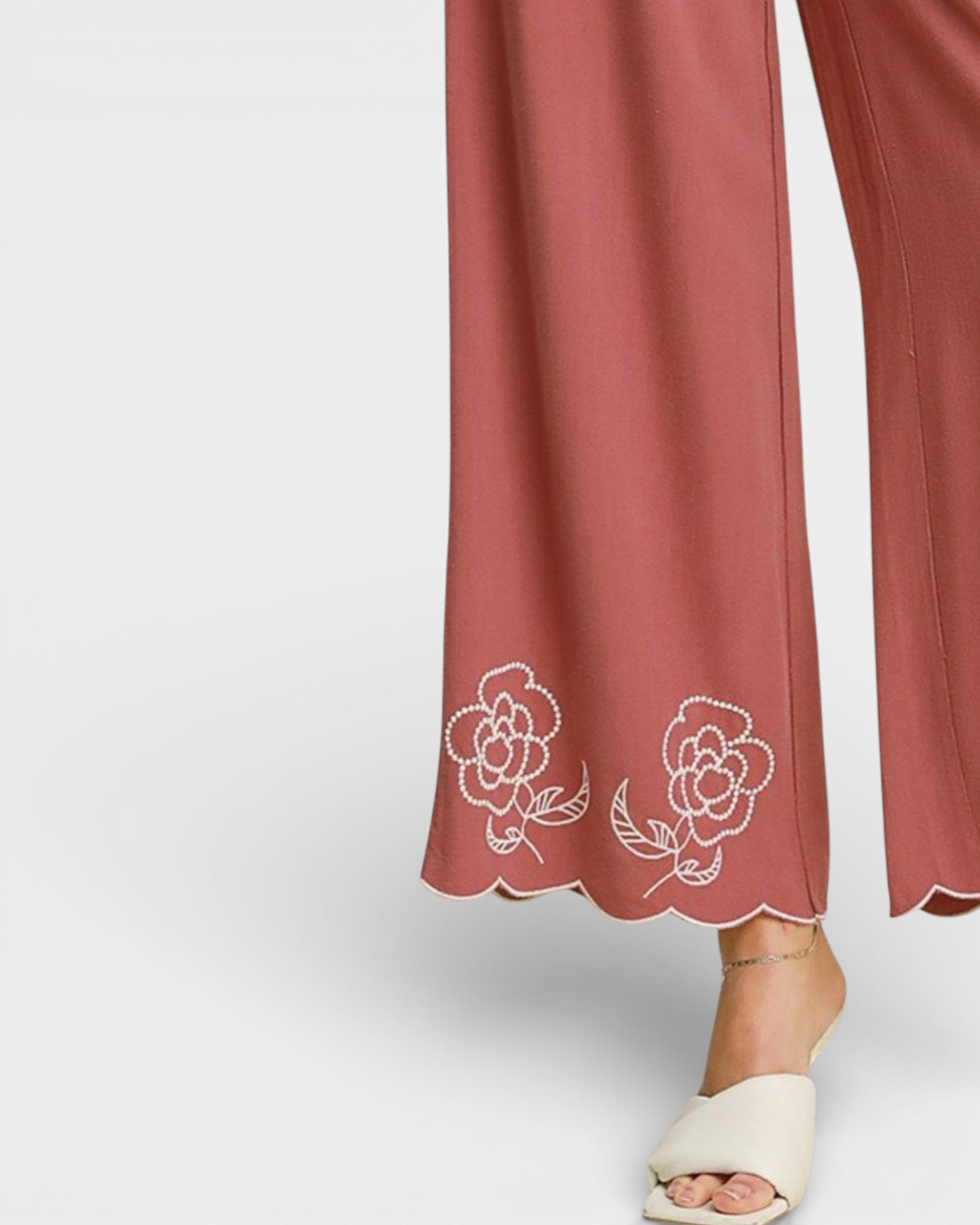 Rose-colored pants with floral embroidery on a light gray background