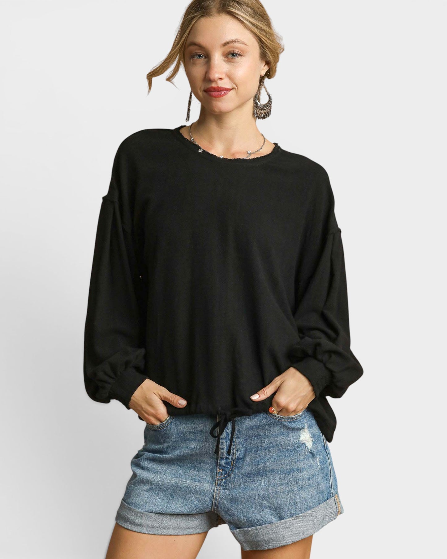 Woman wearing a black long-sleeve top and denim shorts on a white background