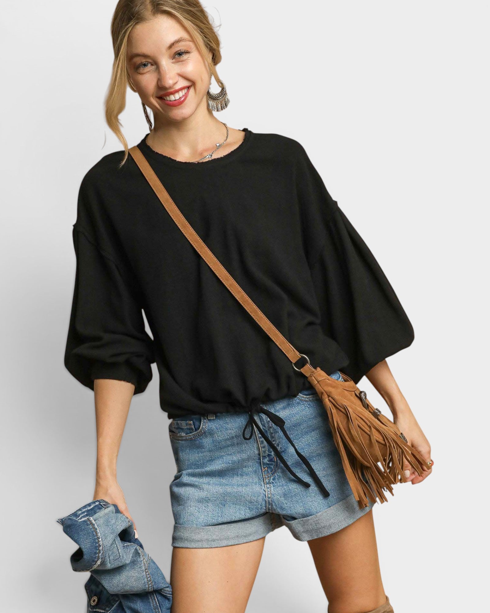 Woman wearing a black sweater and denim shorts with a brown leather bag on a white background