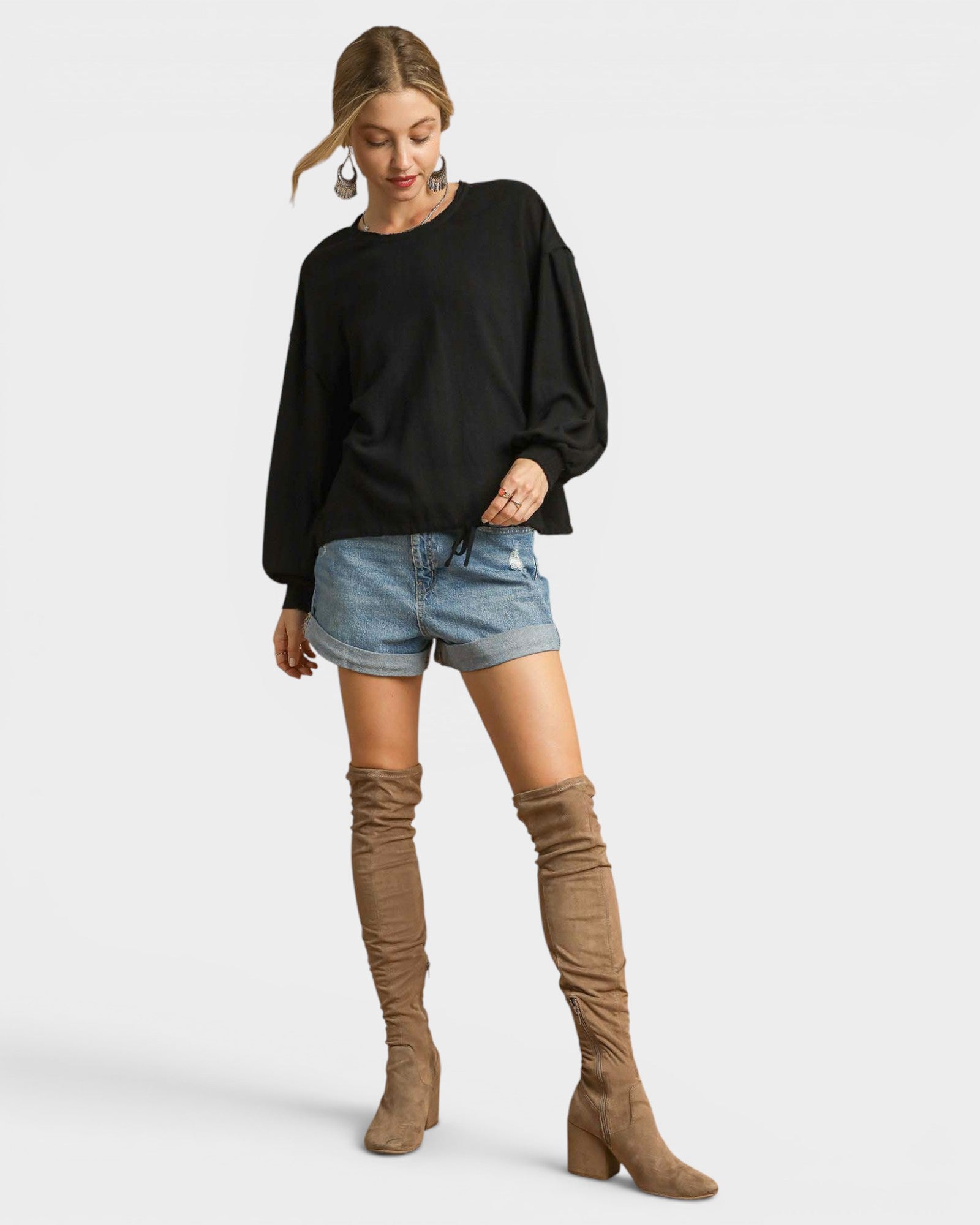 Woman wearing a black sweater, denim shorts, and brown knee-high boots on a white background