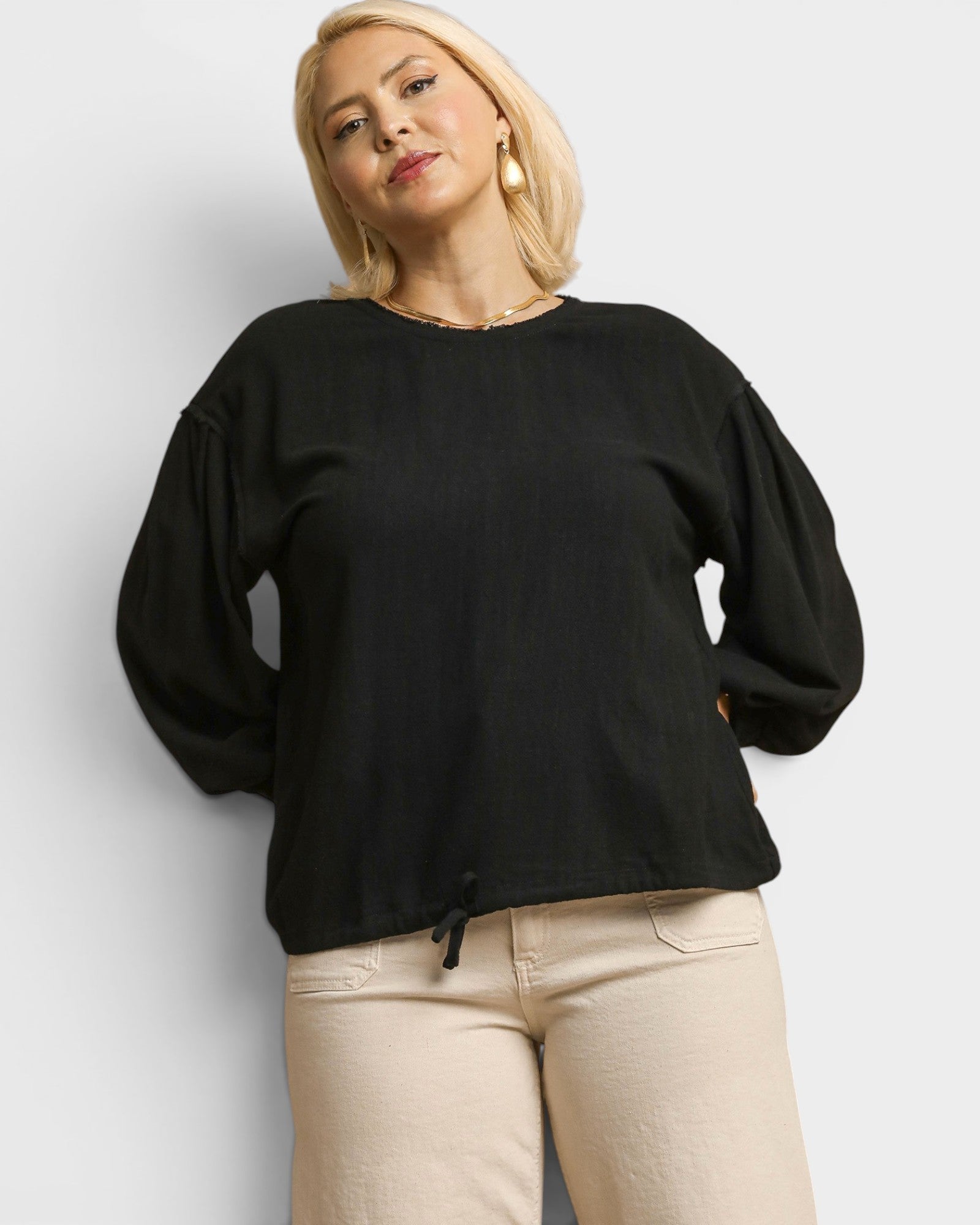 Woman wearing a black sweater and beige pants against a white background