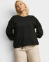 Woman wearing a black sweater and beige pants against a white background