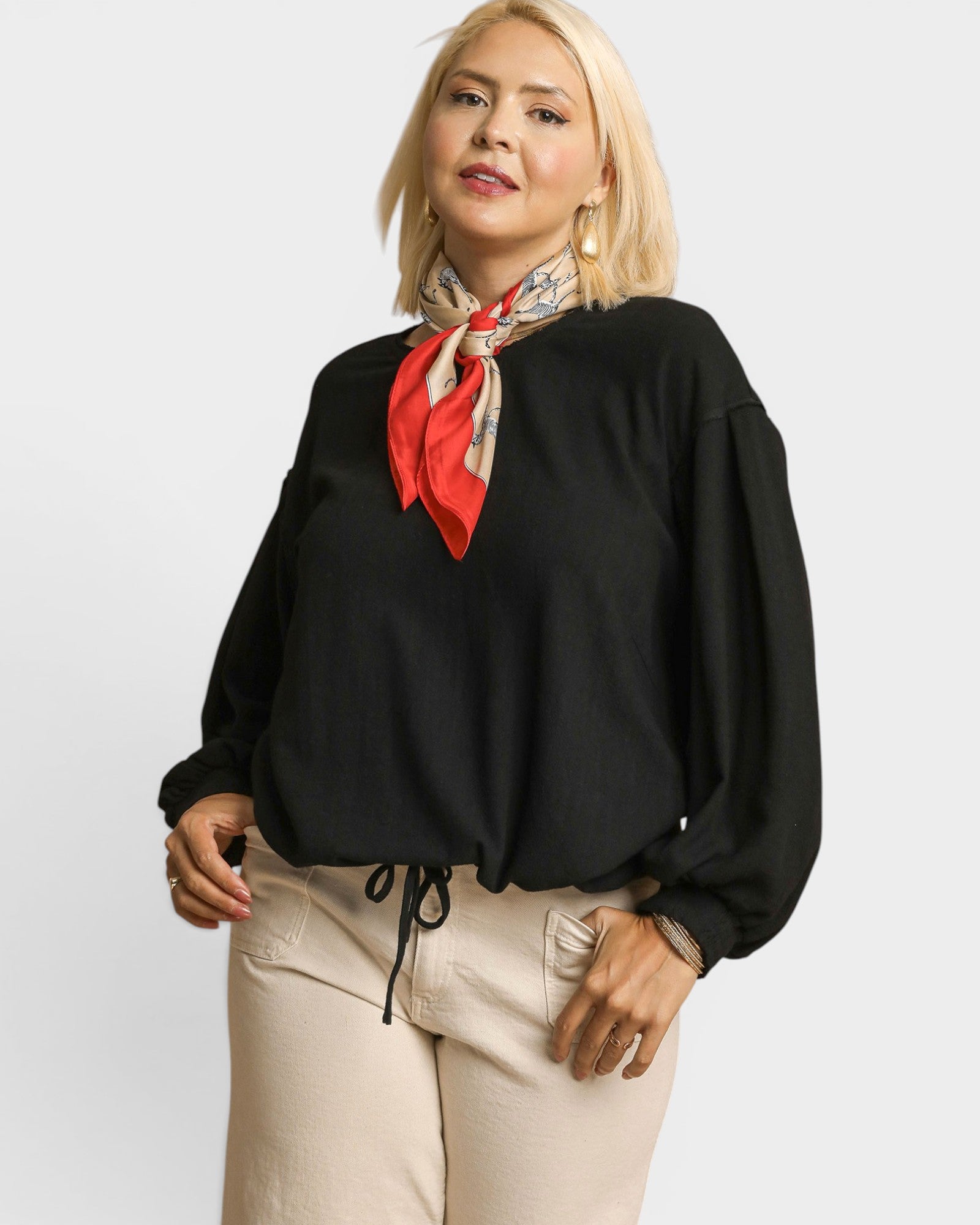 Woman wearing a black top with a red scarf and beige pants on a white background