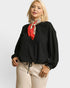 Woman wearing a black top with a red scarf and beige pants on a white background