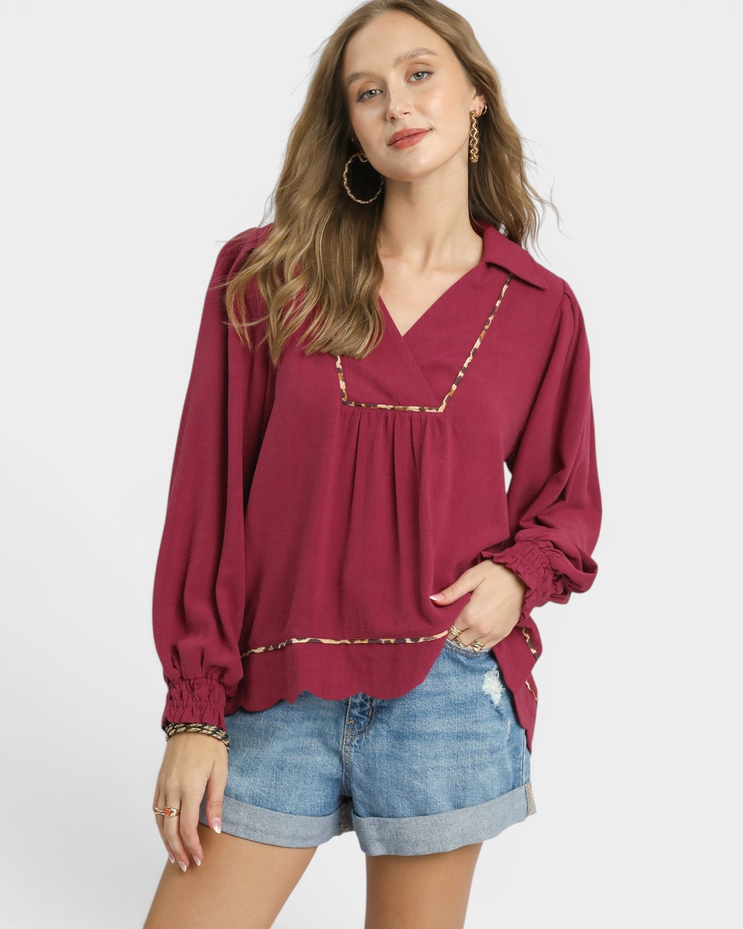 Woman wearing a burgundy blouse with long sleeves and denim shorts on a white background