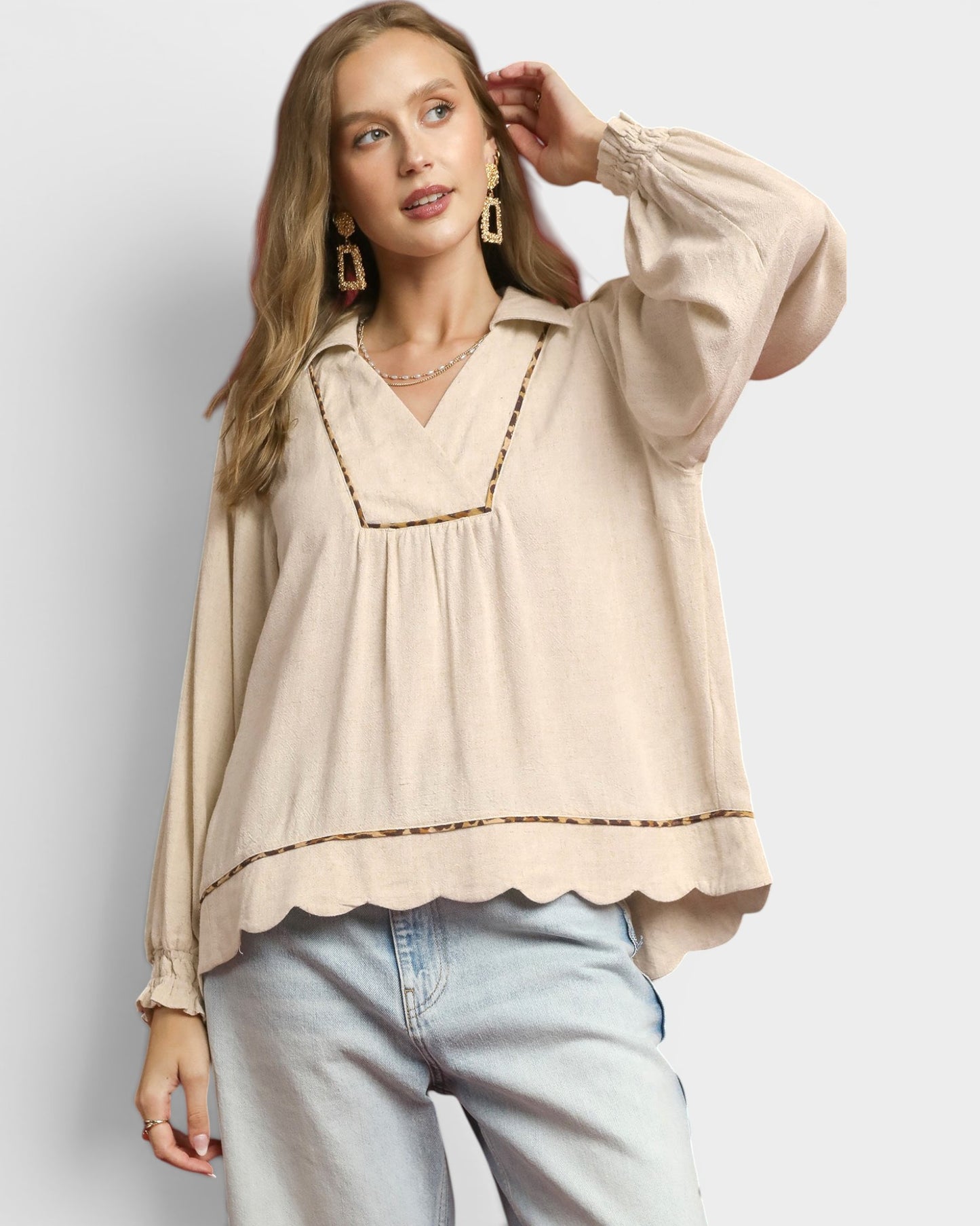 Woman wearing a beige blouse with scalloped edges and light blue jeans on a plain background