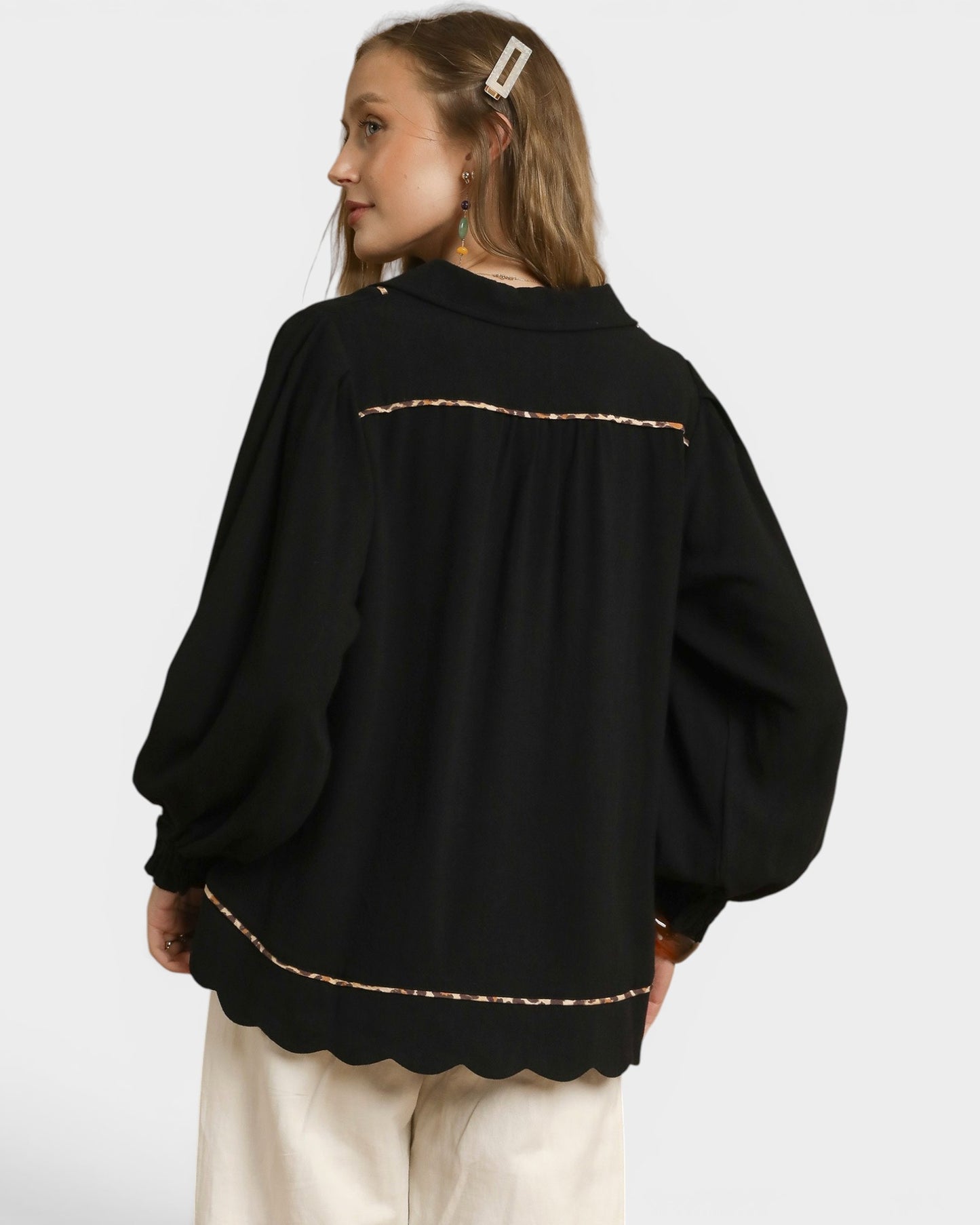 Person wearing a black sweater with scalloped hem on a white background