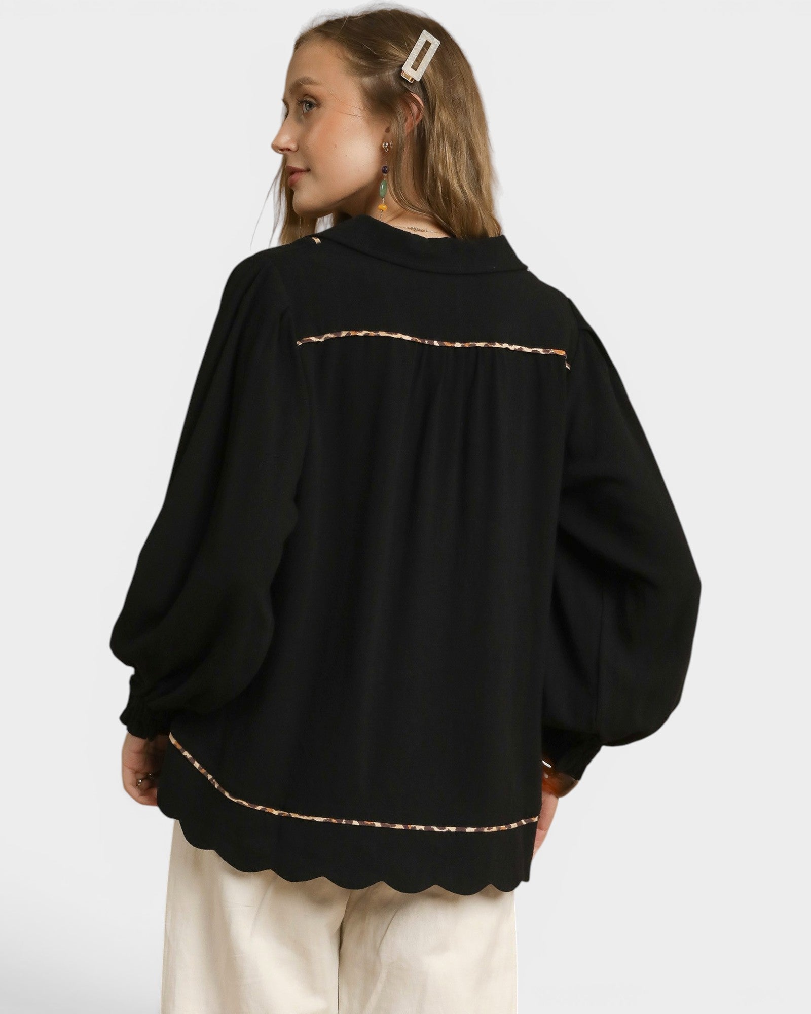 Person wearing a black sweater with scalloped hem on a white background