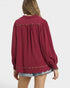 Red blouse with scalloped trim worn by a person on a white background