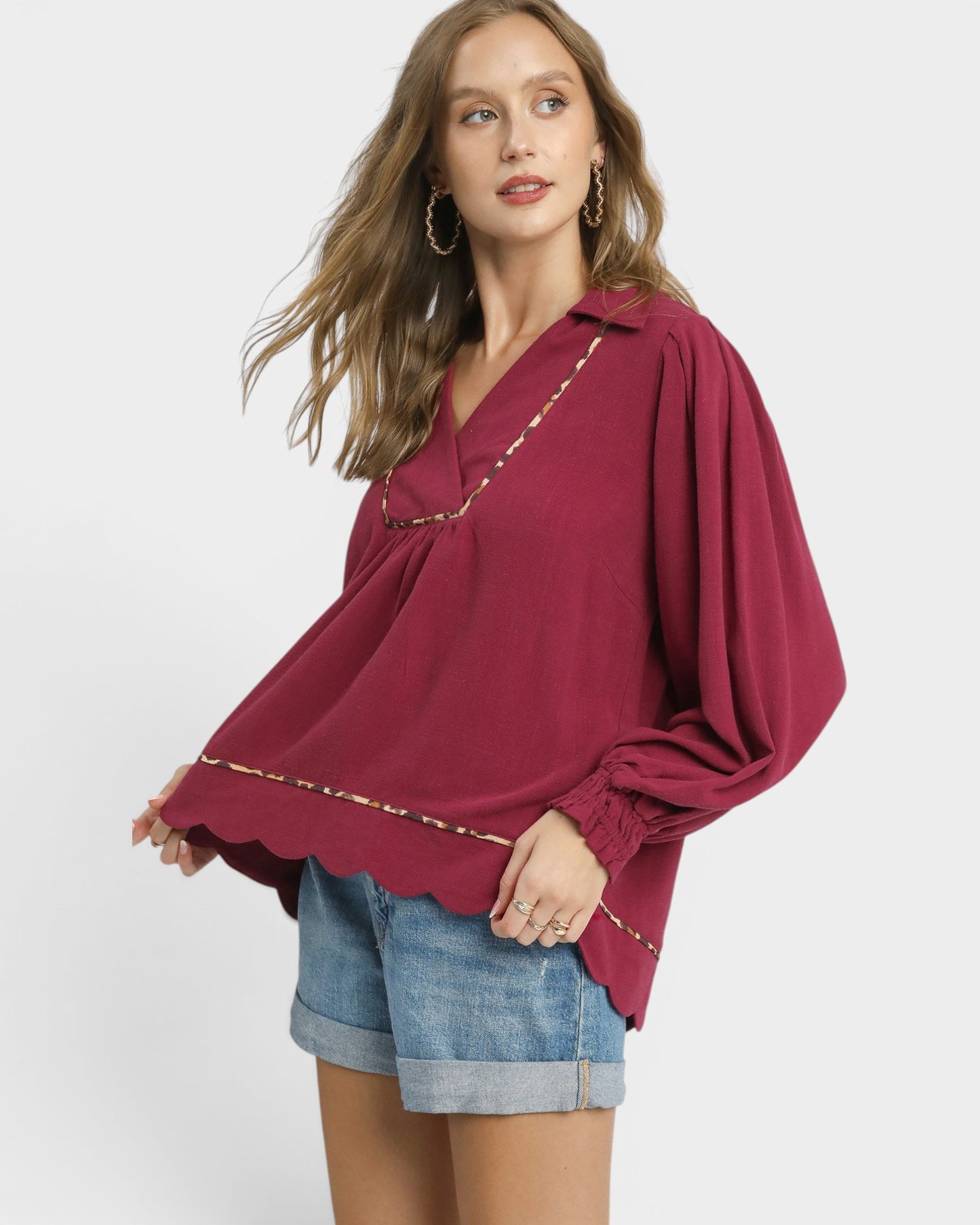 Woman wearing a burgundy blouse with gold trim on a white background