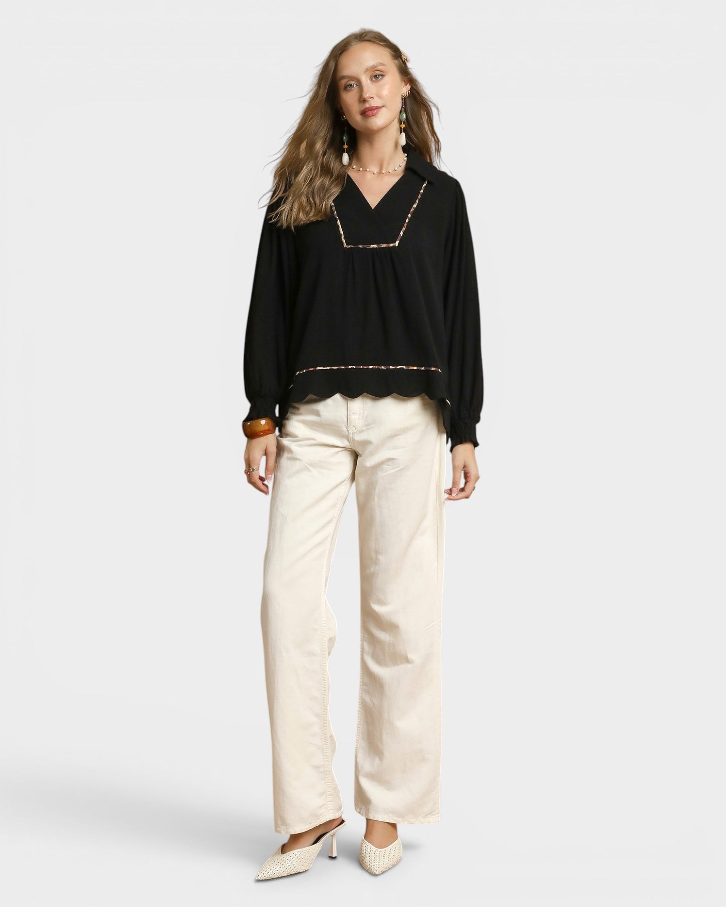 Woman wearing a black blouse with gold trim and beige pants on a white background