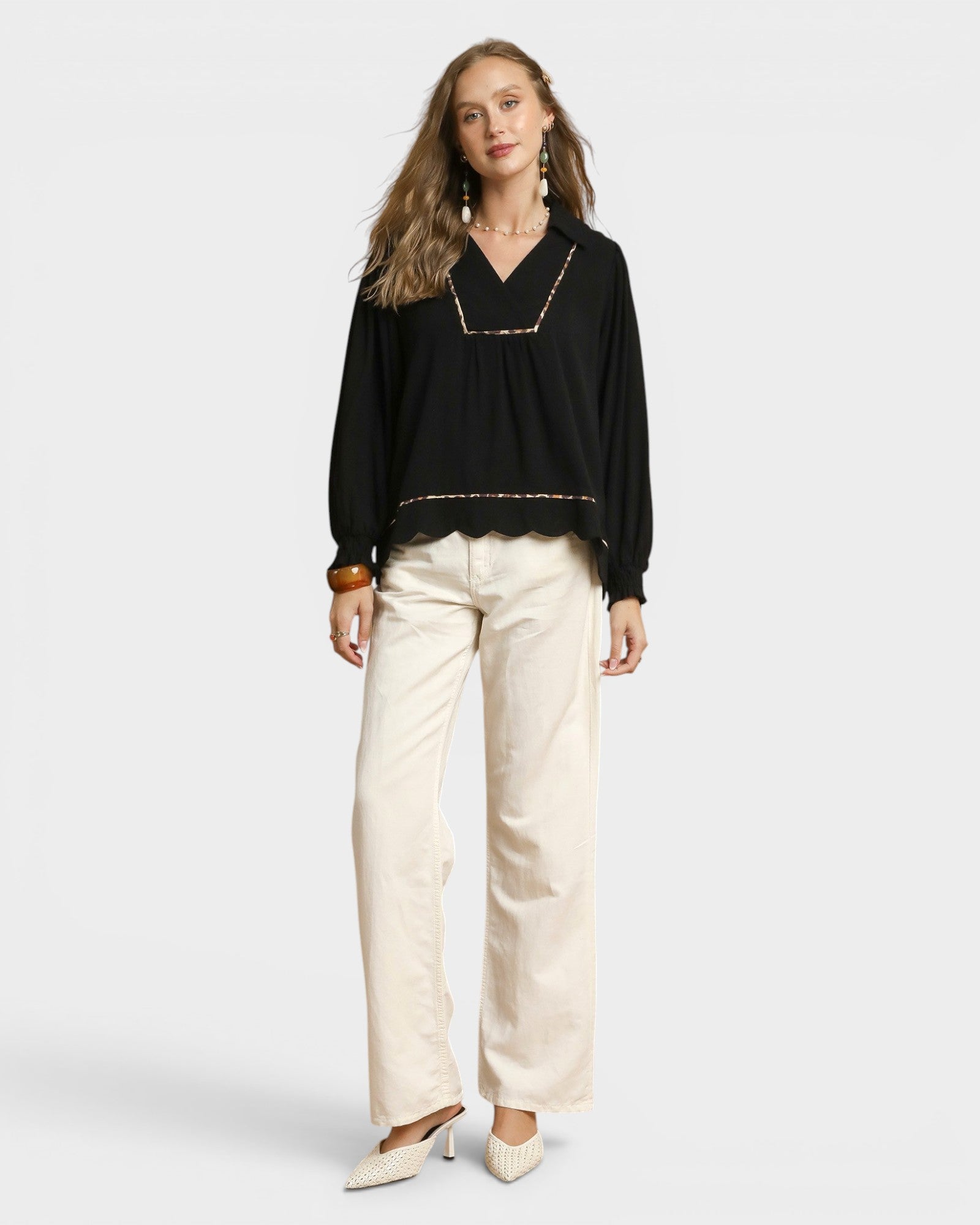 Woman wearing a black blouse with gold trim and beige pants on a white background