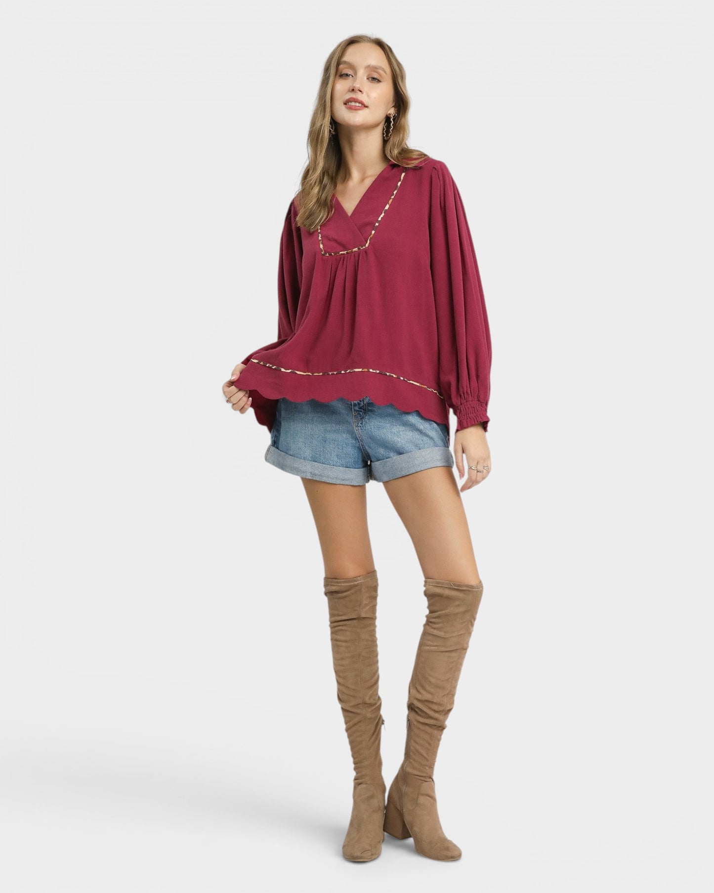 Woman wearing a burgundy top and denim shorts with brown knee-high boots on a white background