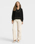 Woman wearing a black blouse with gold trim and beige pants on a white background