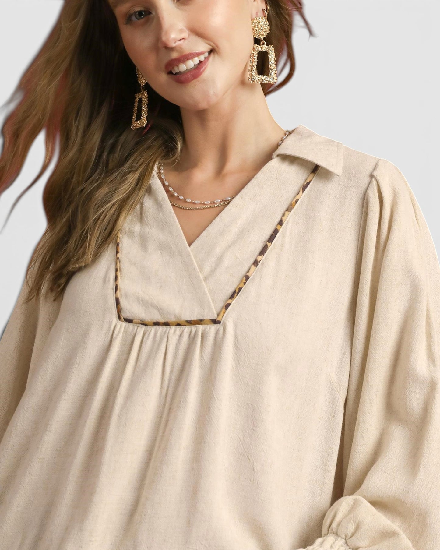 Woman wearing a beige blouse with a necklace and earrings on a light background
