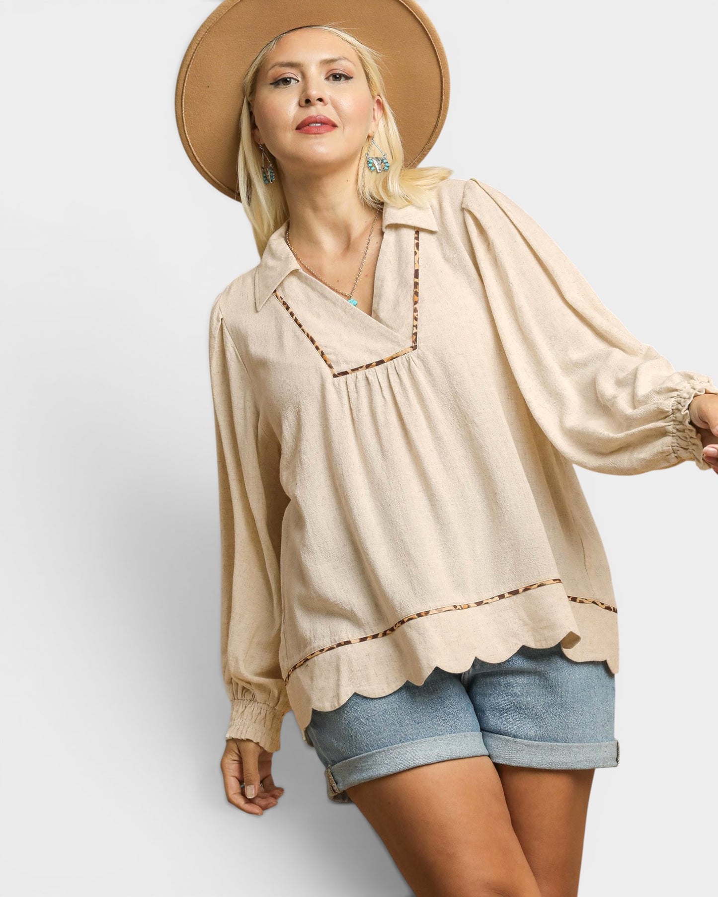 Woman wearing a beige blouse with scalloped edges and denim shorts on a white background