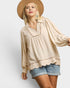 Woman wearing a beige blouse with scalloped edges and denim shorts on a white background