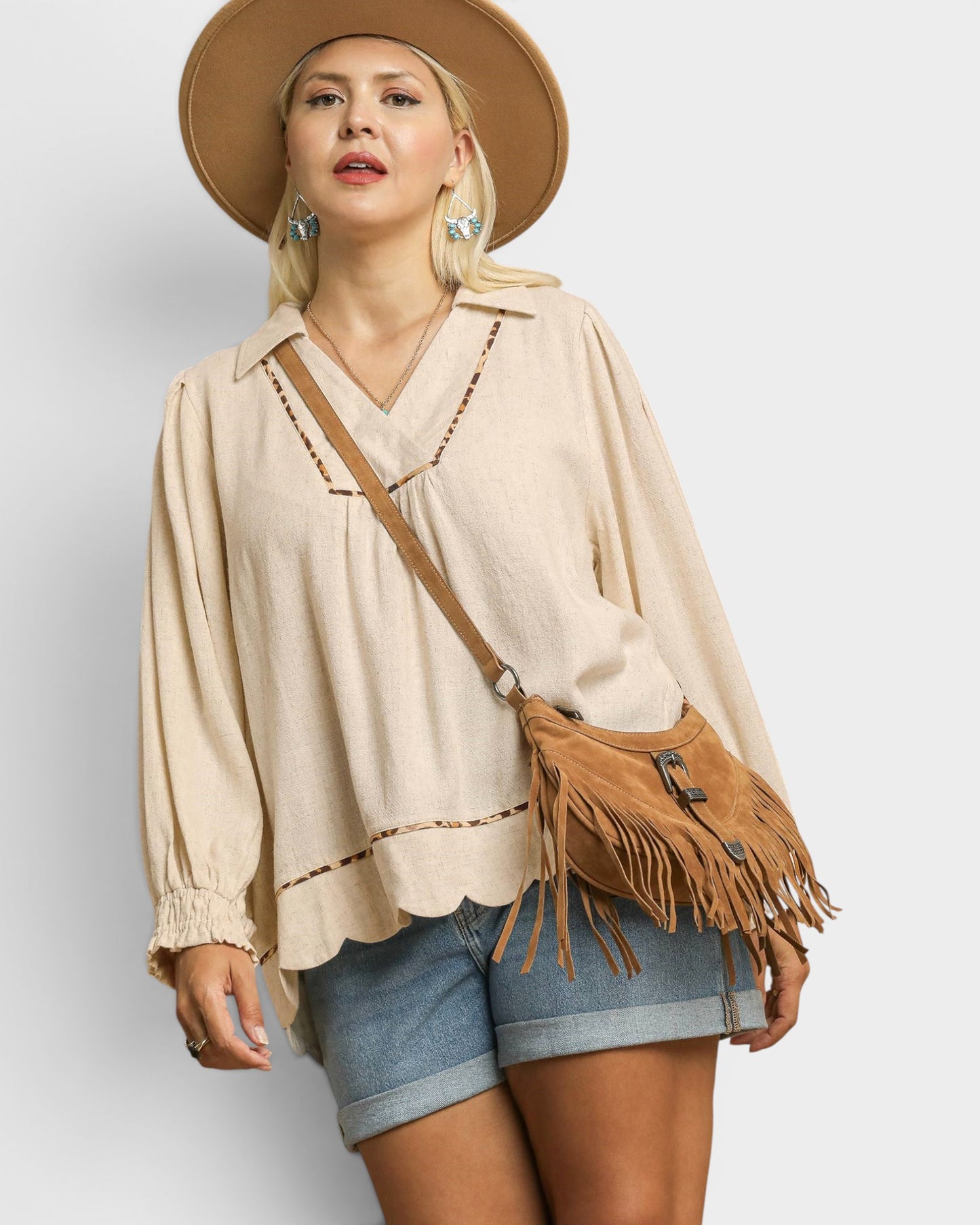 Woman wearing a beige blouse, denim shorts, and a brown hat with a matching bag on a light gray background
