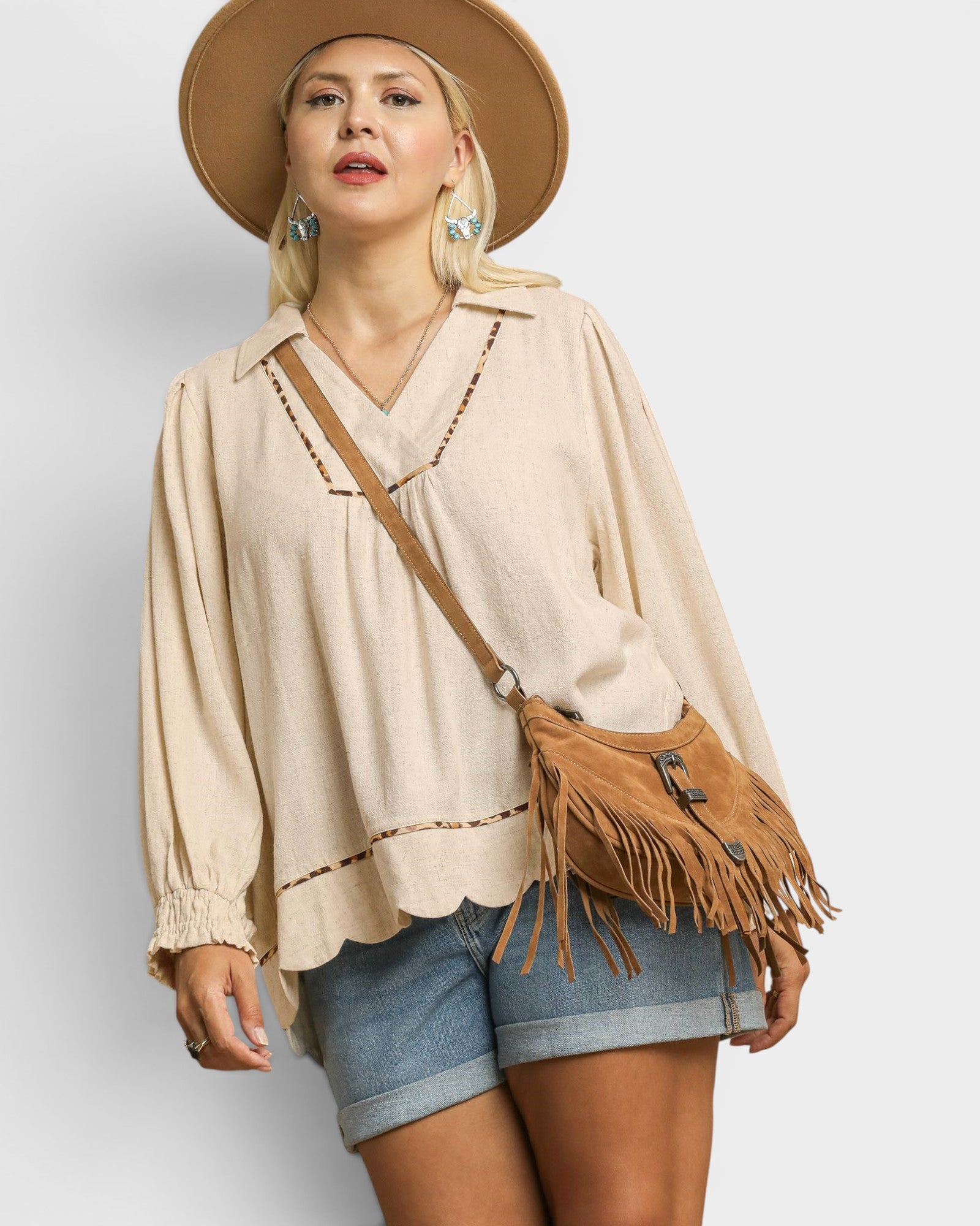 Woman wearing a beige blouse, denim shorts, and a brown hat with a matching bag on a light gray background