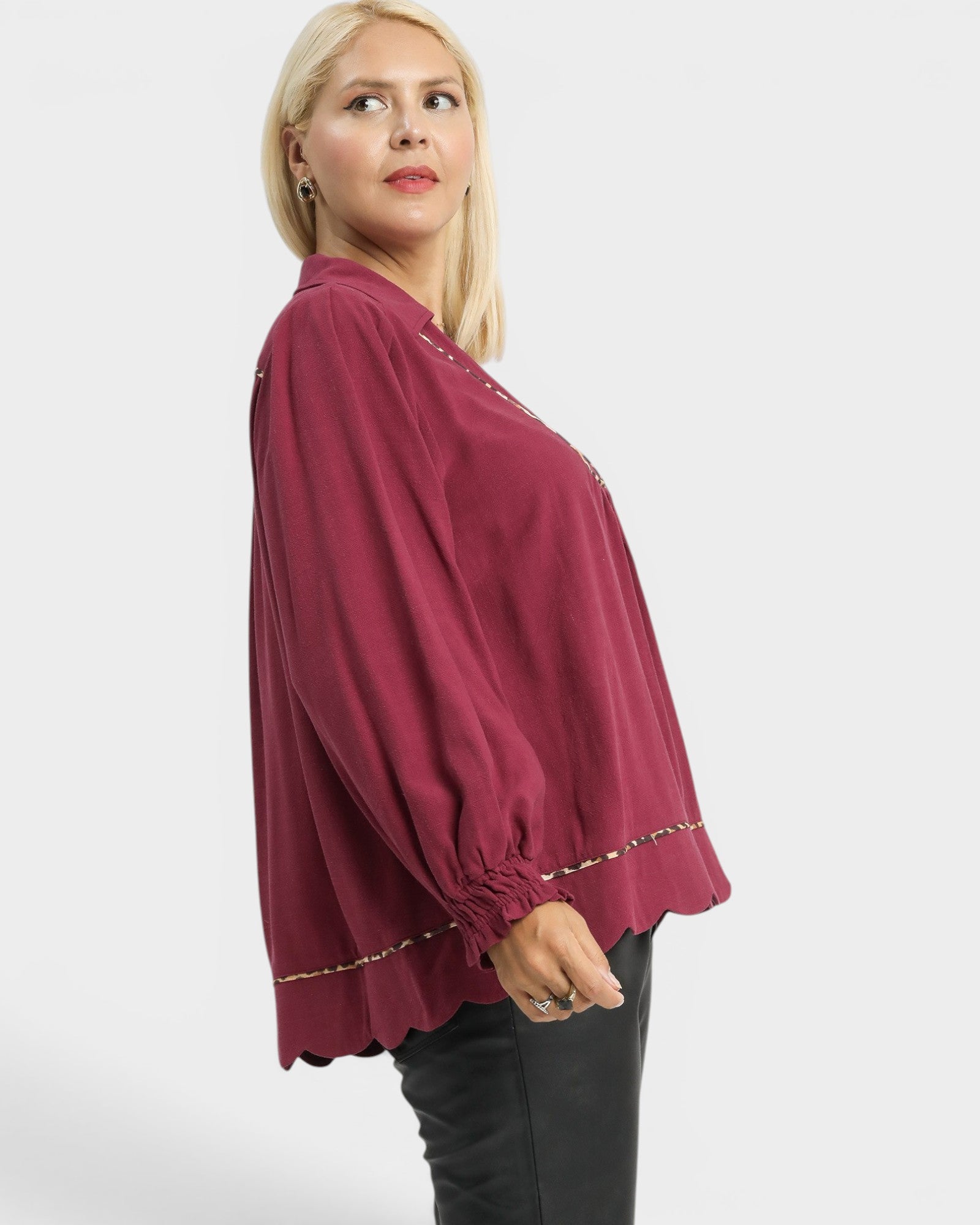 Woman wearing a burgundy blouse with gold trim on a white background
