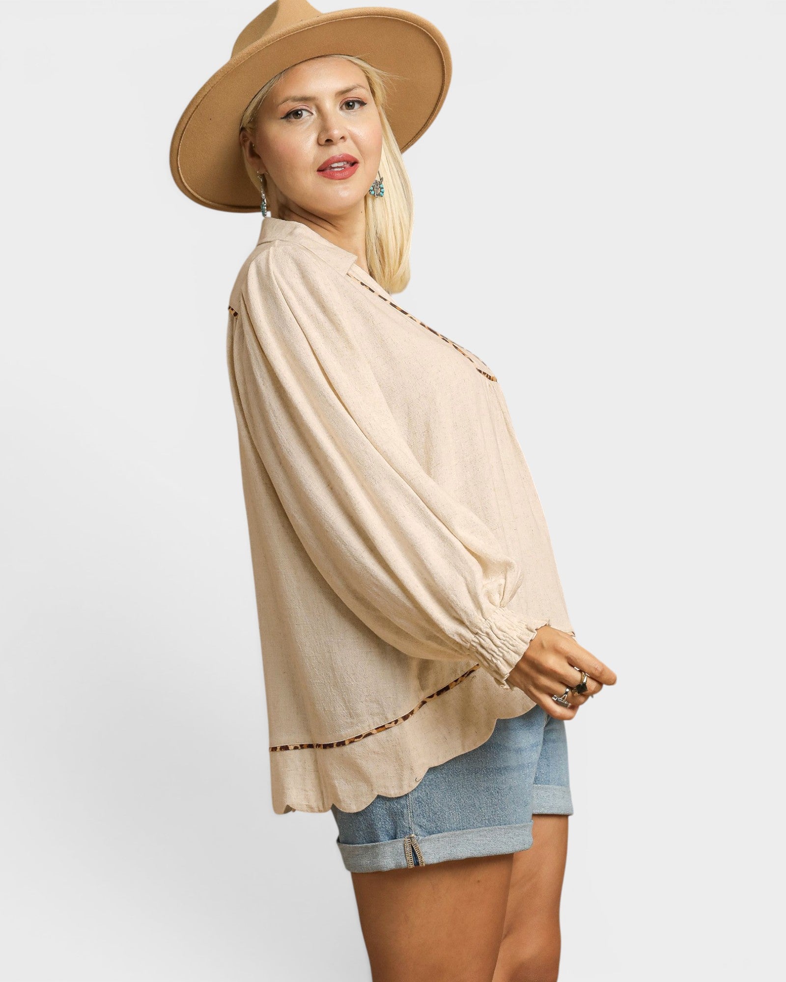 Woman wearing a beige top, denim shorts, and a beige hat on a white background