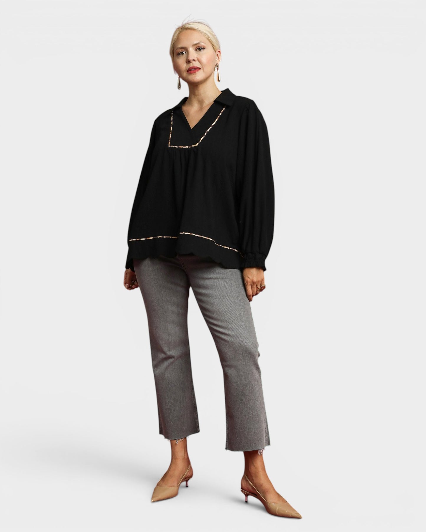 Woman wearing a black top with gold trim and gray pants on a white background