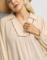 Woman wearing a beige blouse with a necklace and hat against a neutral background