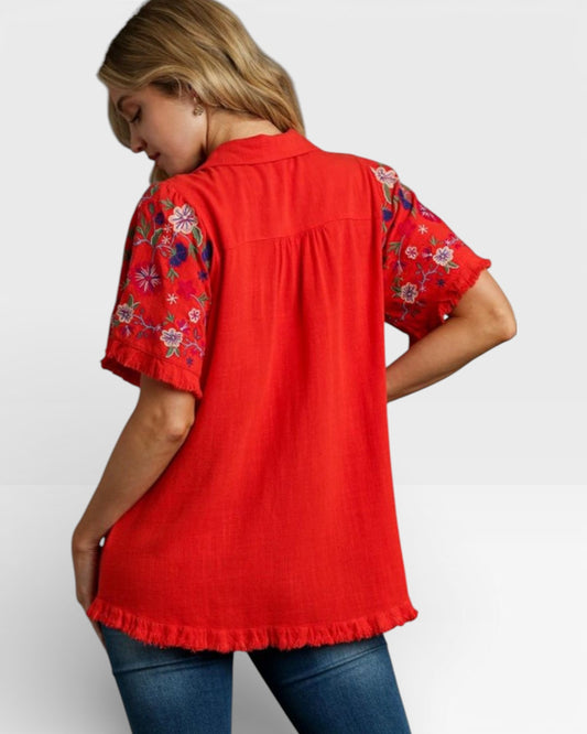 Red blouse with floral sleeves worn by a person on a white background