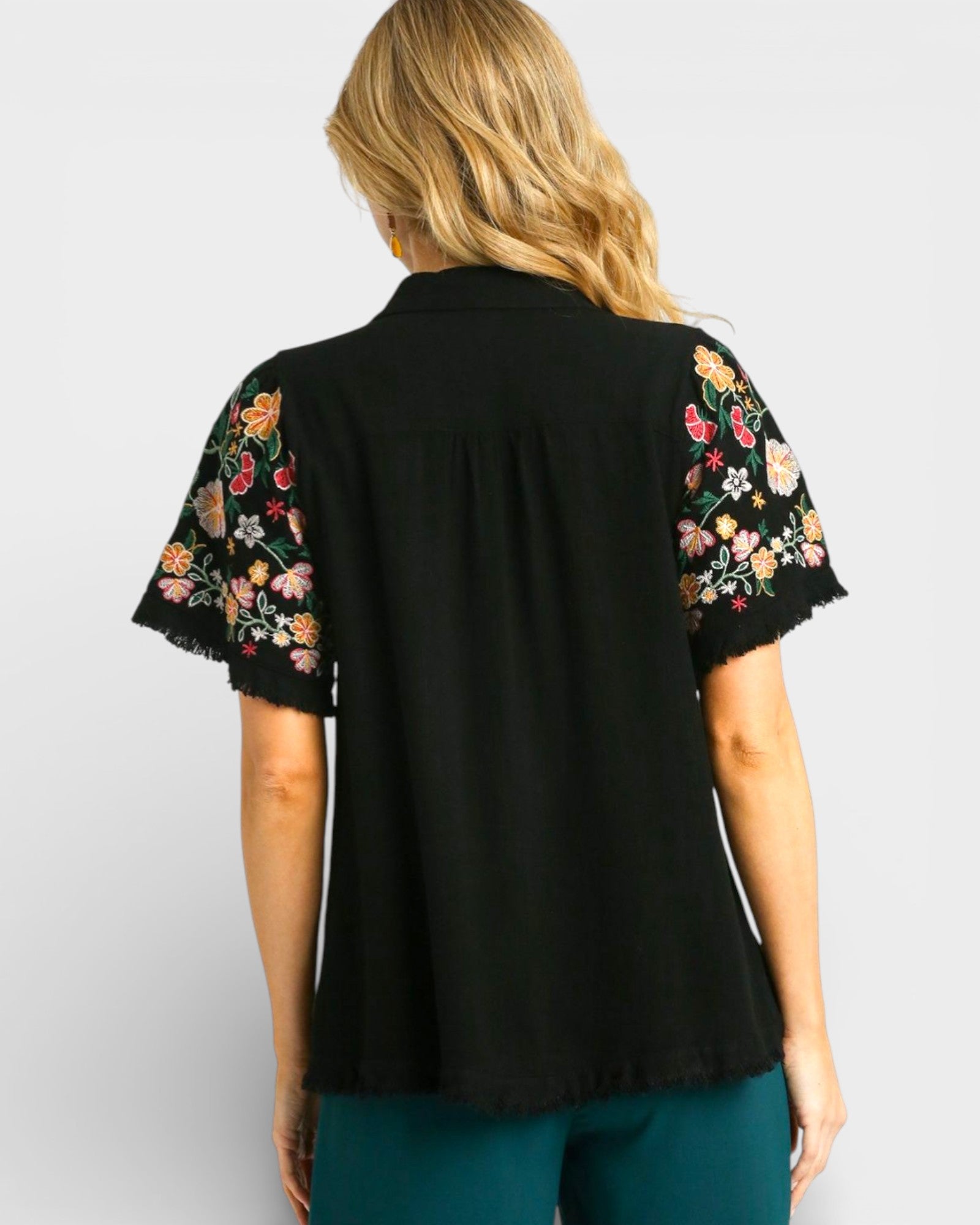 Black blouse with floral embroidery on sleeves worn by a person against a light gray background