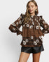 Woman wearing a brown floral blouse and black shorts on a white background