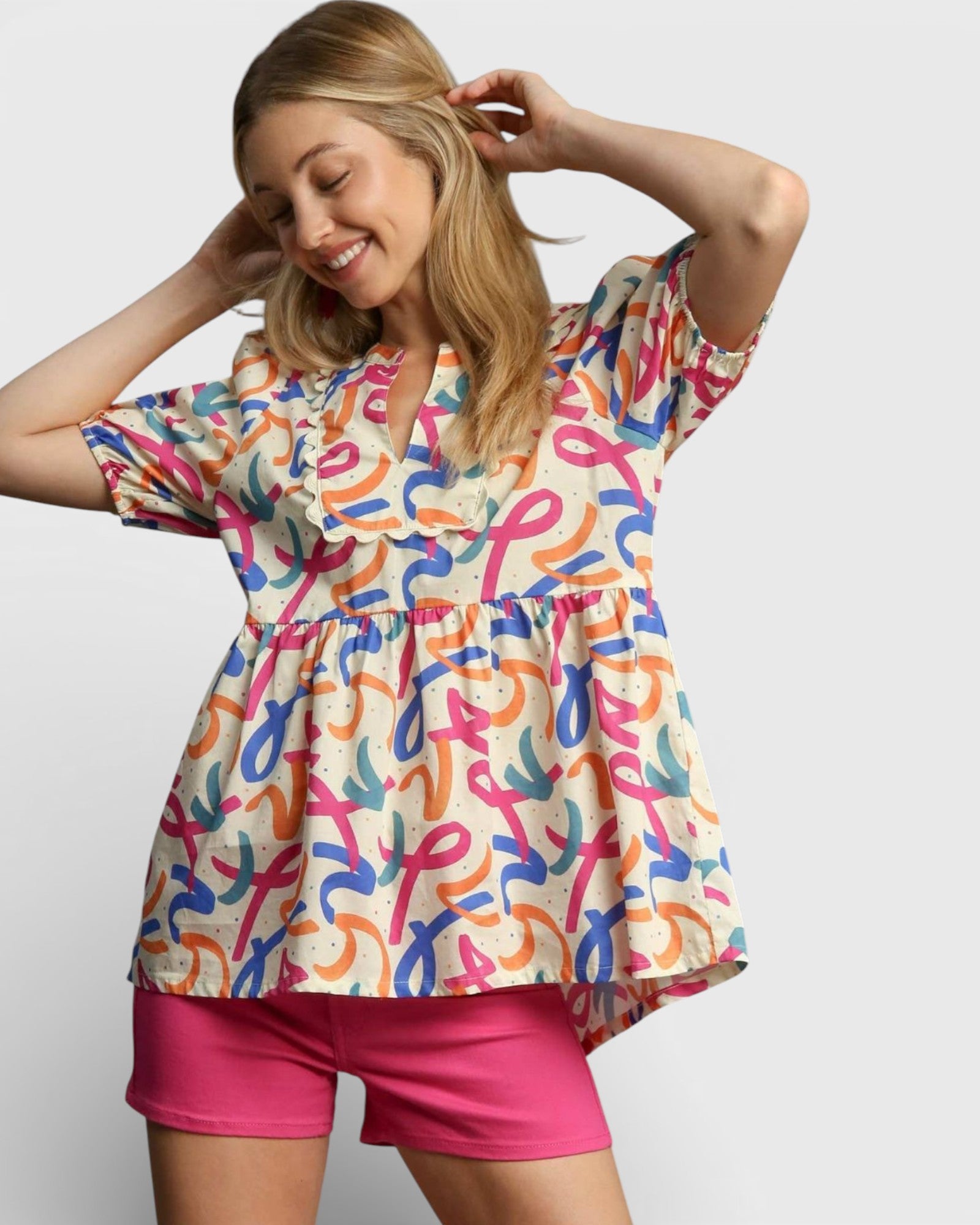 Woman wearing a colorful patterned top and pink shorts on a plain background