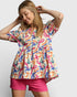 Woman wearing a colorful patterned top and pink shorts on a plain background