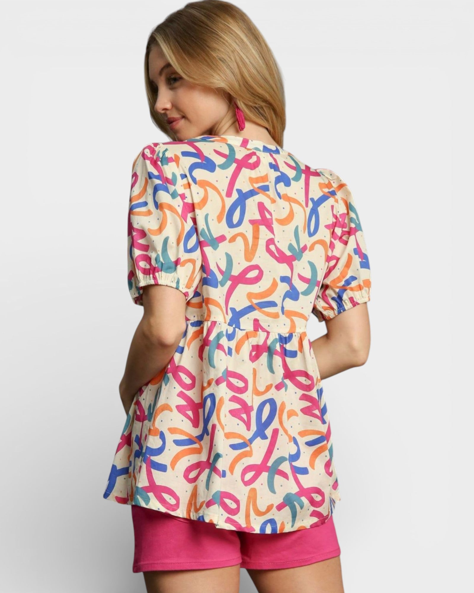 Woman wearing a colorful patterned shirt with pink shorts on a white background