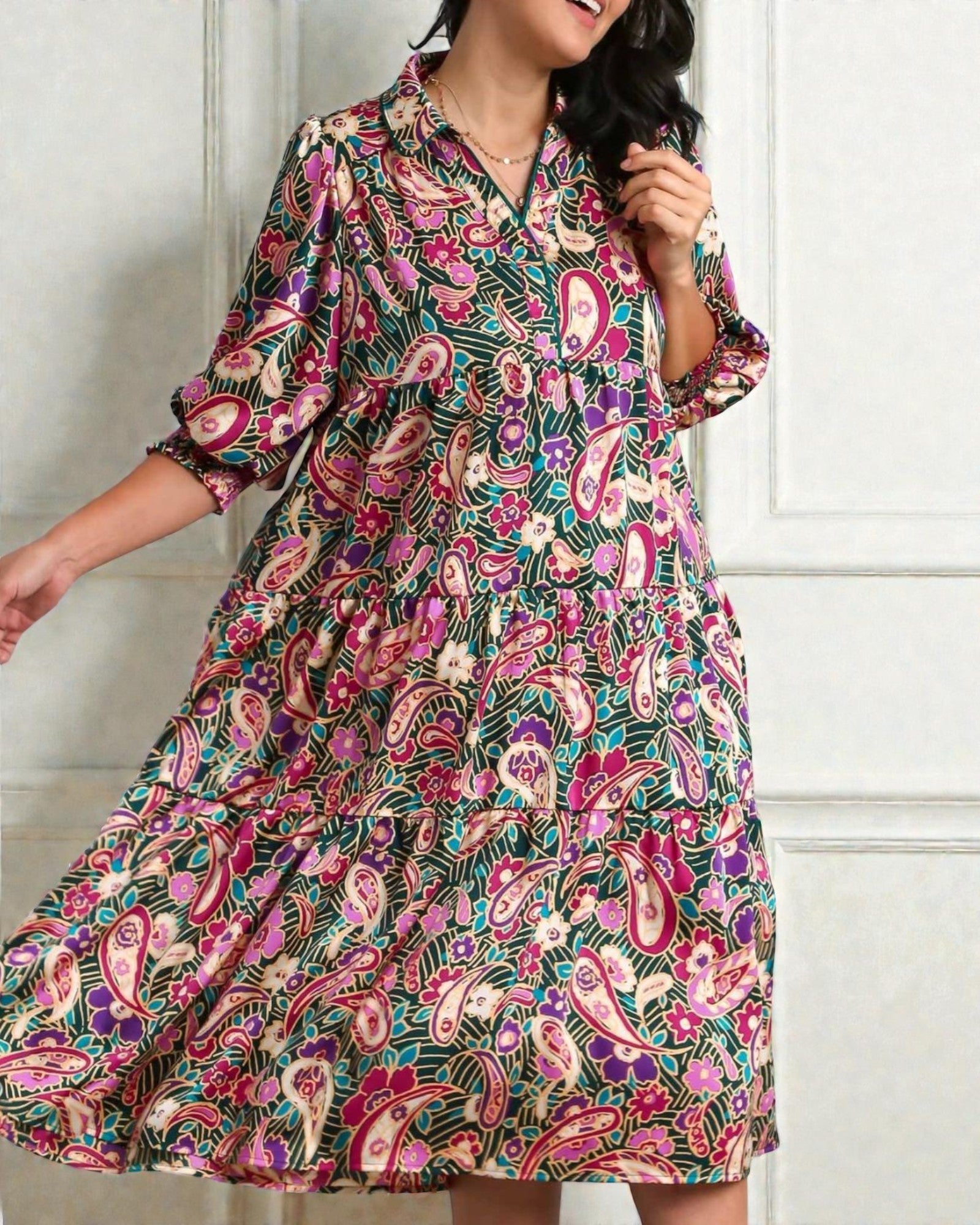 Woman wearing a colorful paisley dress against a white wall.