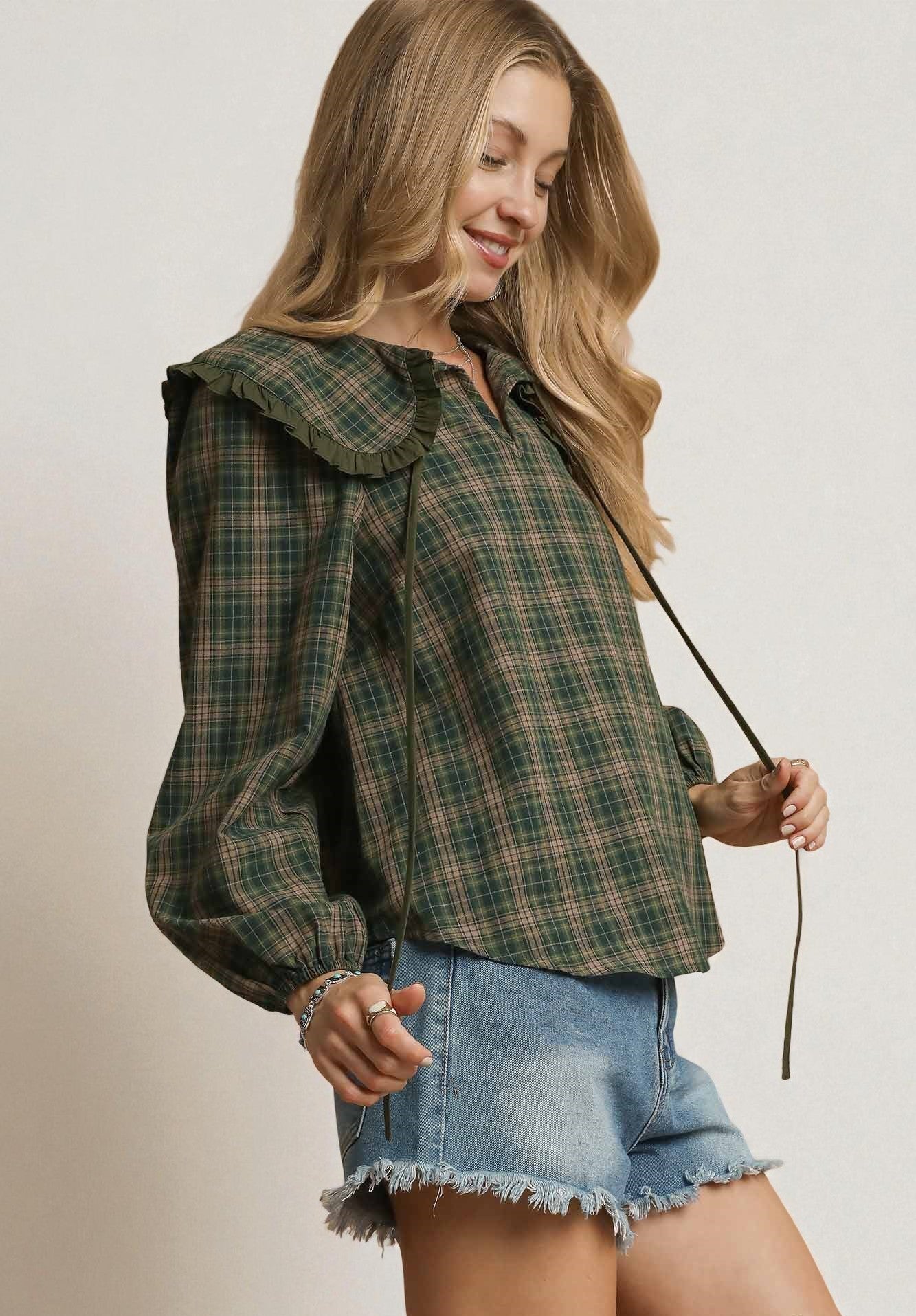 Woman wearing a plaid jacket and denim shorts holding a walking stick against a plain background