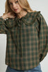 Woman wearing a green plaid shirt with a ruffled collar on a white background