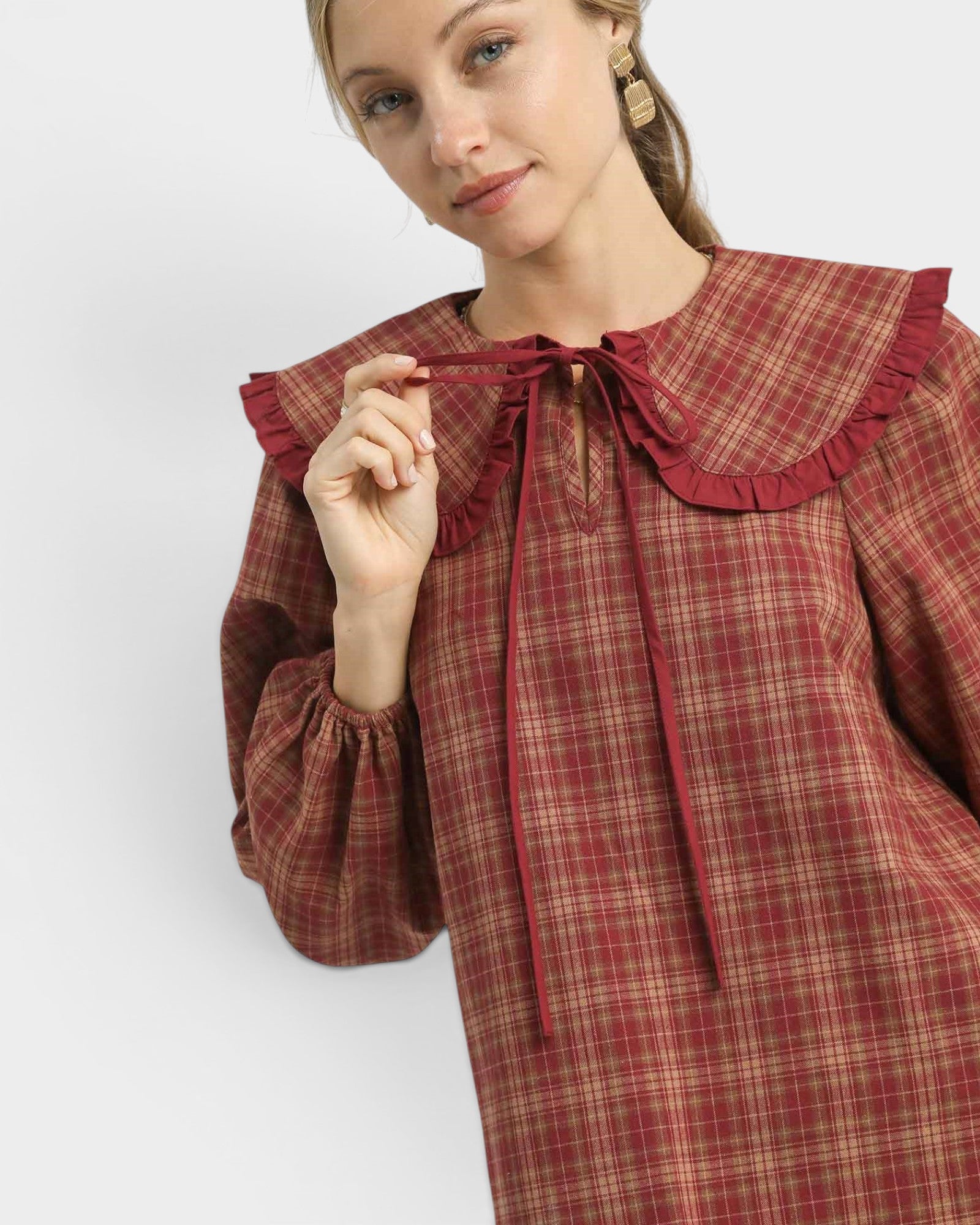 Woman wearing a red plaid dress with a ruffled collar against a white background