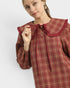 Woman wearing a red plaid dress with a ruffled collar against a white background
