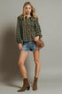 Woman wearing a plaid shirt, denim shorts, and brown boots with a brown bag against a gray background