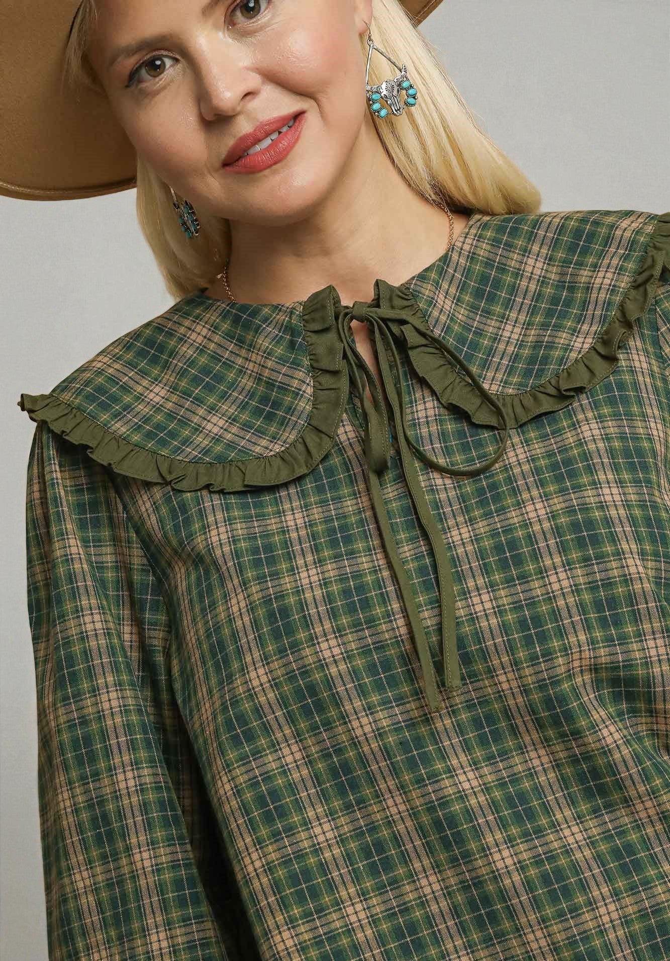 Woman wearing a green plaid dress with a ruffled collar against a gray background