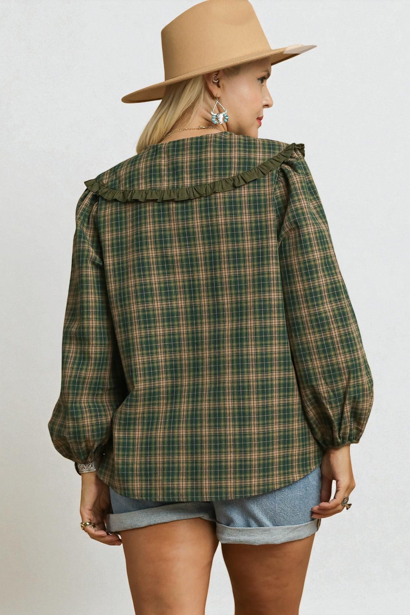 Person wearing a green plaid shirt and beige hat on a plain background