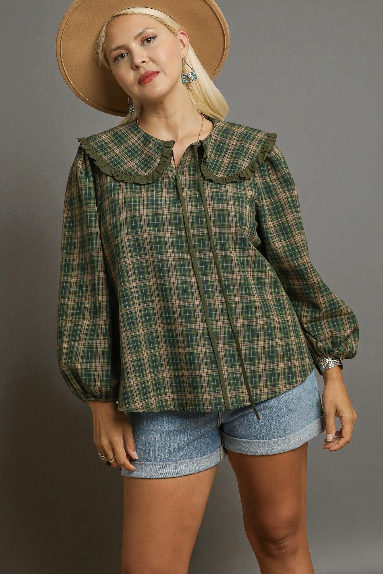 Woman wearing a green plaid shirt and denim shorts against a gray background
