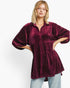 A woman modeling a deep burgundy velvet tunic top with a subtle gold polka dot pattern, paired with light blue jeans against a plain white studio background.