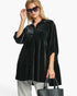 A woman modeling a black velvet long-sleeve tunic top with small white polka dots, styled with gray pants, black sunglasses, and a black tote bag against a plain white background.