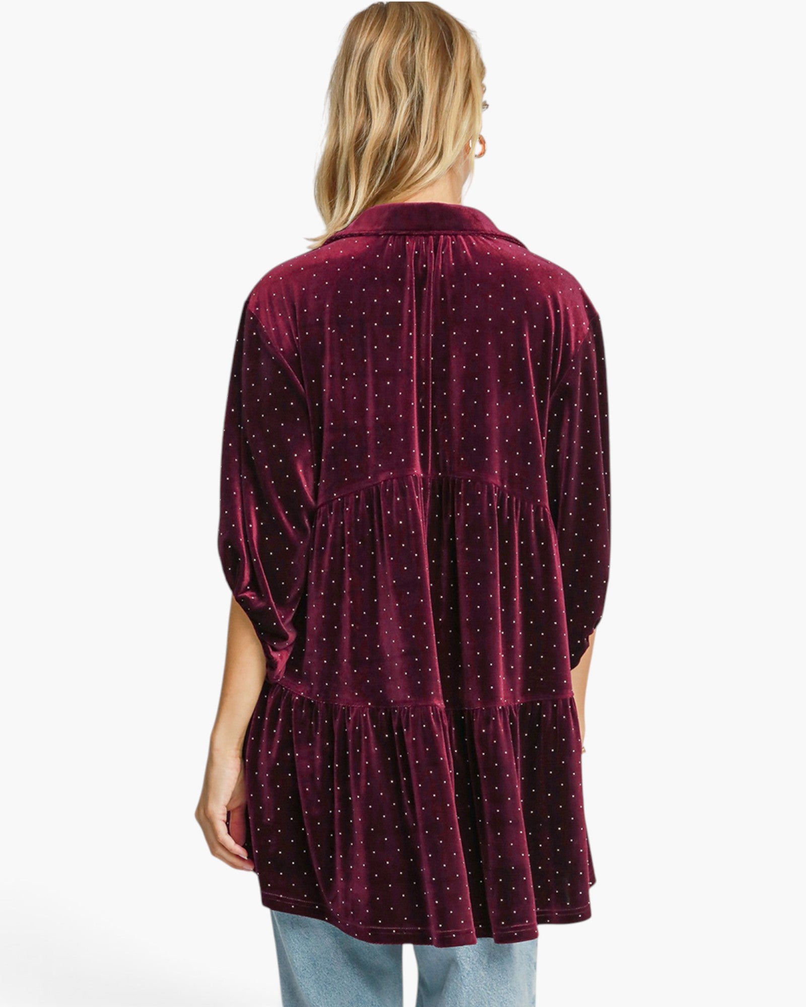 A woman shown from the back wearing a deep burgundy velvet tiered tunic top with a small white polka dot pattern, paired with light blue jeans, against a plain white background.