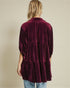Person wearing a burgundy velvet dress with a subtle pattern on a beige background