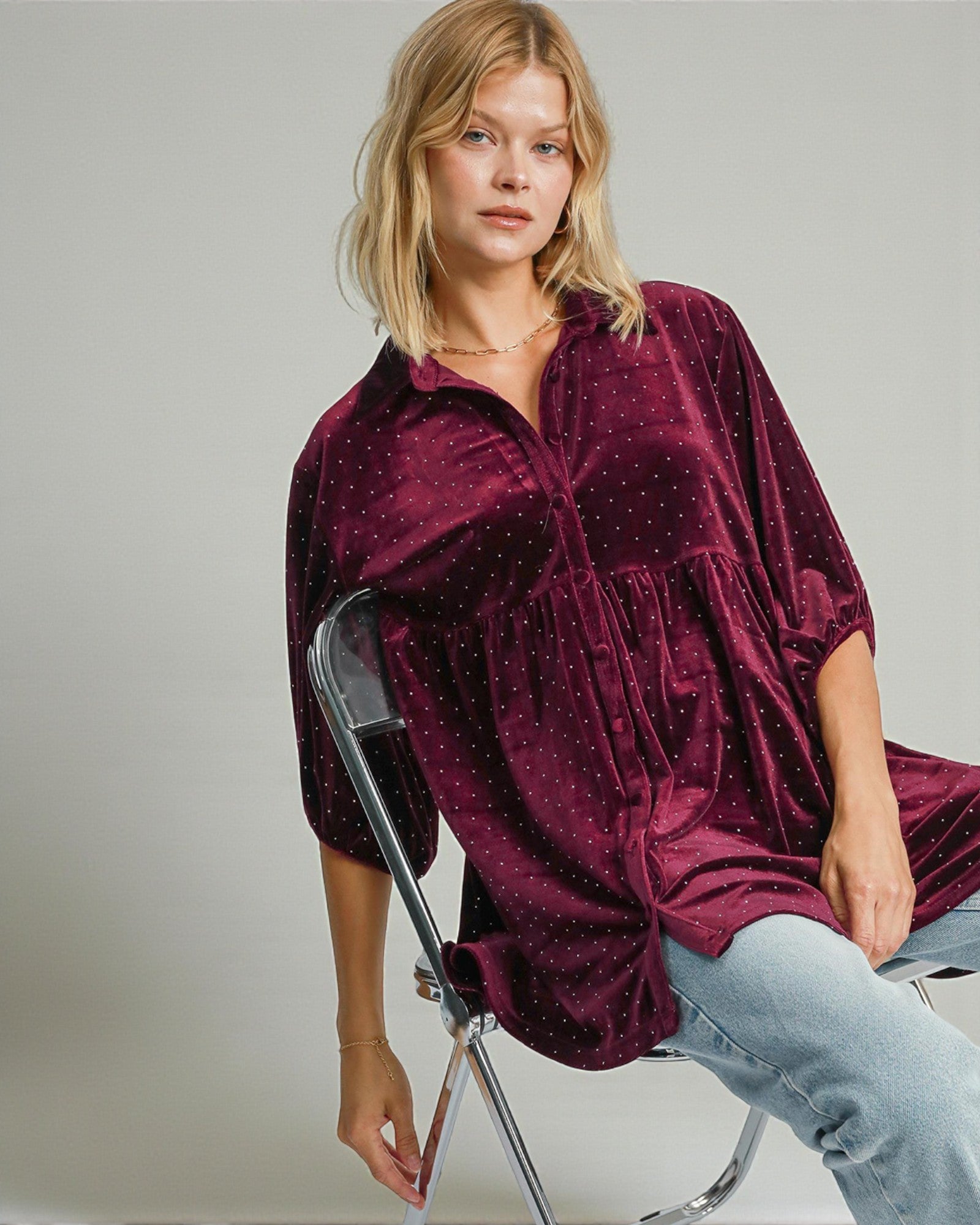 Woman wearing a burgundy velvet shirt sitting on a chair against a plain background