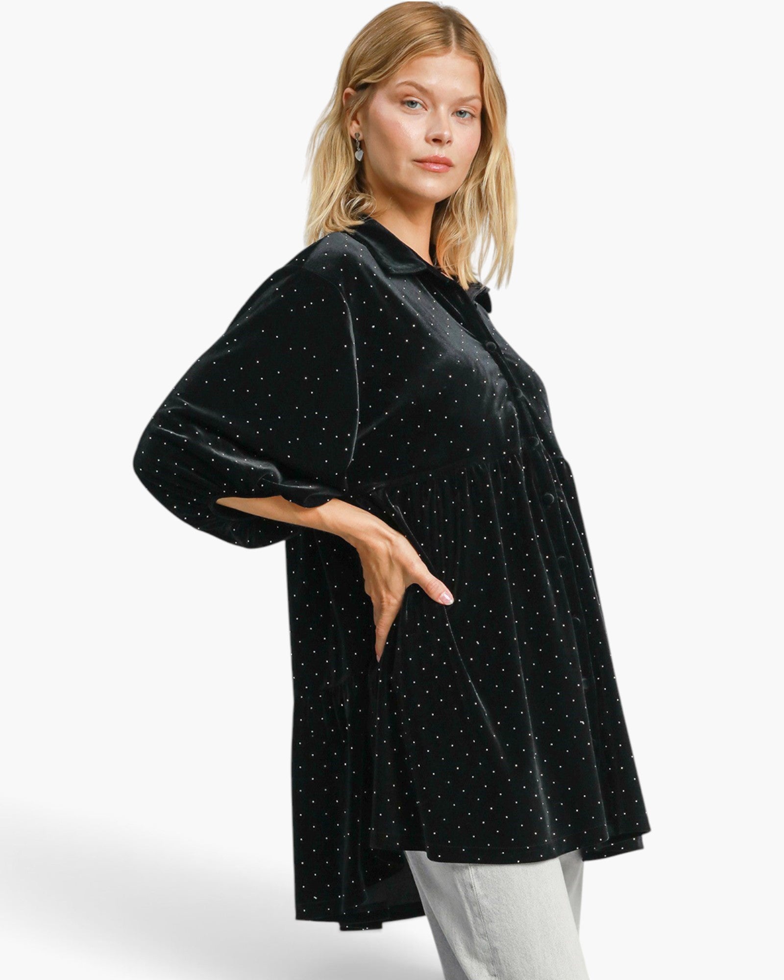 A woman modeling a black velvet button-up shirt jacket with small white polka dots, paired with light gray pants, against a plain white studio background.