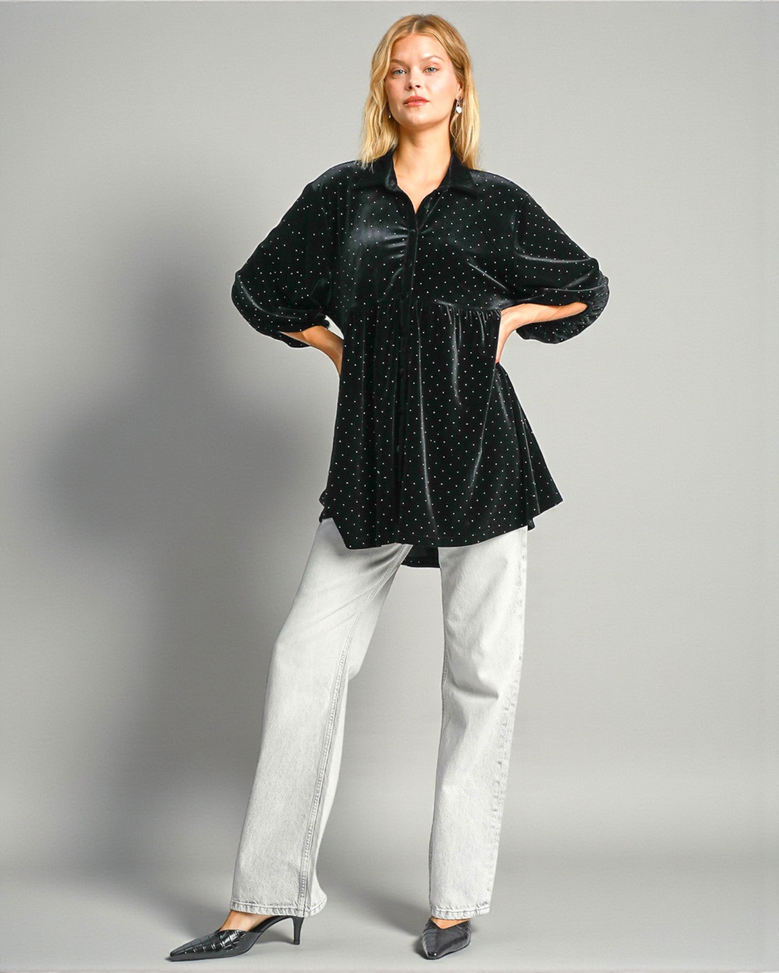 Woman wearing a black patterned blouse and white pants on a gray background