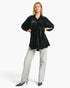 A woman modeling a black velvet long-sleeve blouse with small white polka dots, paired with light gray wide-leg jeans and black pointed-toe heels, against a plain white studio background.